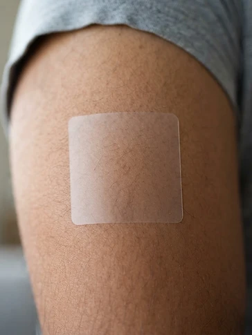 Close-up macro photograph of a transparent PACHEEZ patch adhered to adult upper arm skin showing natural pores