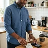 Adult man in his 40s placing PACHEEZ packet on kitchen bench beside phone and keys before work