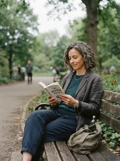 Woman in her late 40s sitting relaxed on a park bench in soft overcast morning light