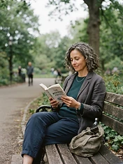 Woman in her late 40s sitting relaxed on a park bench in soft overcast morning light