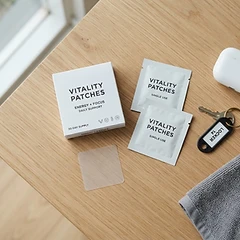 Overhead flat lay of PACHEEZ product box, patch sachets and one transparent patch on a natural timber surface beside gym towel and earbuds