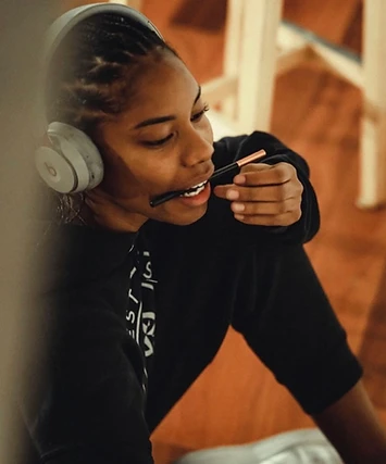 Close-up portrait of Anaïa holding a stylus between her teeth, wearing headphones