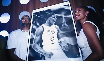 Two figures holding a framed charcoal portrait of a USA basketball player