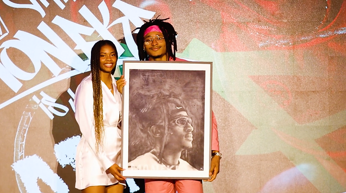 Anaïa and a subject holding a framed charcoal portrait before a graffiti wall