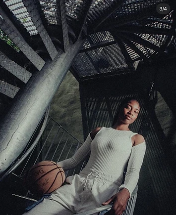 Anaïa seated beside a metal spiral staircase, holding a basketball
