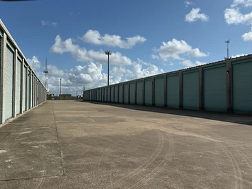 Wide paved drive aisle between rows of drive-up storage units at Challenger Storage in Webster, TX
