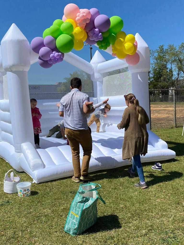 Family playing at white bounce house with balloon arch