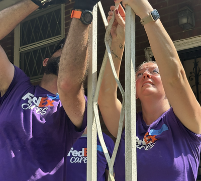 Volunteers repairing a porch railing on a brick home