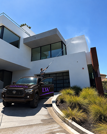 A LuxWash Co. technician soft washing a modern home, with the branded company truck parked in the driveway