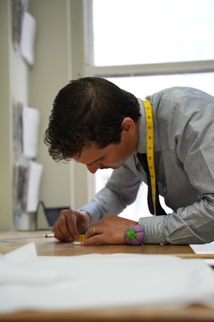 A tailor at his workbench, drawing a client’s pattern by hand