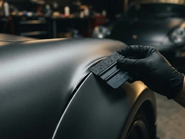 Macro detail of vinyl wrap being smoothed over a fender curve