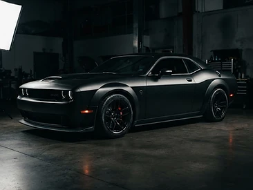 Matte black vinyl wrapped muscle car in a dark studio