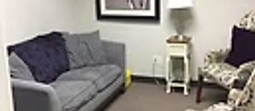 Consultation room corner with a grey sofa, accent chairs, and framed botanical art at Oak Brook Counseling & Wellness.