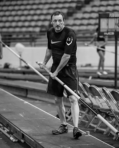 Coach David Brannan on the runway, holding a pole vault pole