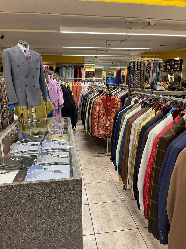 Grey double-breasted suit on a mannequin beside a glass display case with a long rack of suits and sale signage at Paolo Cellini