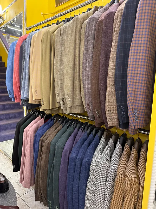 Double row of textured wool and tweed blazers in plaid, tan, and blue hanging on the showroom racks at Paolo Cellini