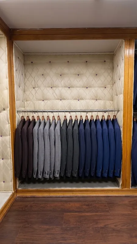 Row of suit jackets arranged by color from brown to blue in a wood-framed alcove with diamond-tufted cream walls at Paolo Cellini