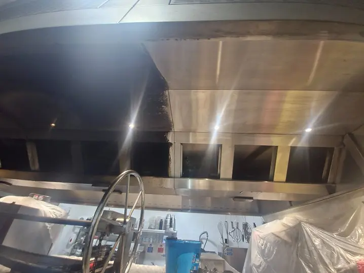 Charcoal grill extraction canopy — left side coated in baked-on carbon, right side cleaned to a reflective stainless-steel finish
