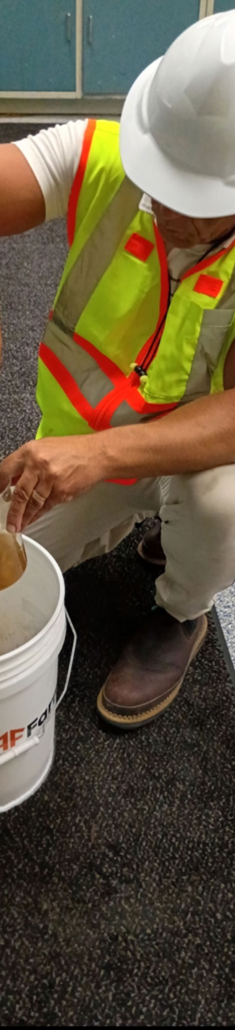 LaNova technician in white hard hat and hi-vis vest pouring coagulant into a beaker during on-site jar trials