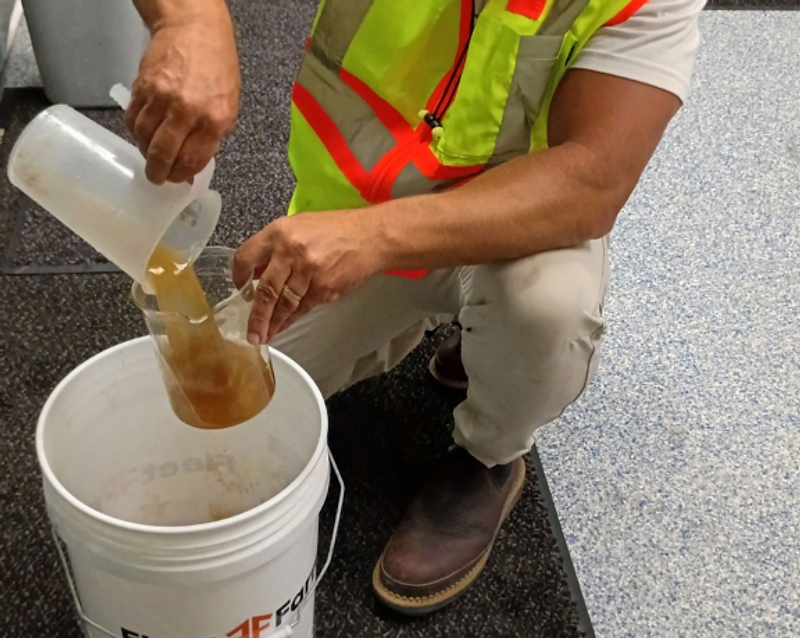 LaNova technician in white hard hat and hi-vis vest pouring coagulant into a beaker during on-site jar trials