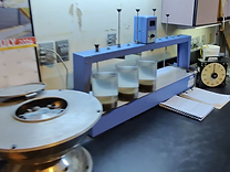 Blue jar-test flocculation apparatus with beakers and a black analog timer on a lab bench