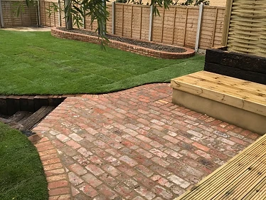 L-shaped seating area with sleeper retaining walls, rustic brick pad flooring, trellis screening, fencing & Indian sandstone paving