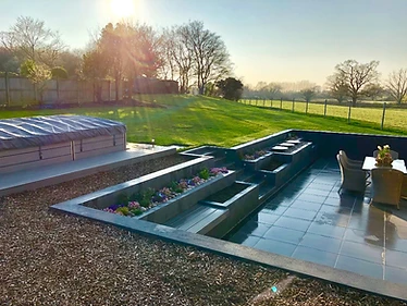 Modern contemporary sunken garden with major retaining works, L-shaped seating area, water table fountains, exterior porcelain, swim spa installation & reclamation of soil to reinstate the field