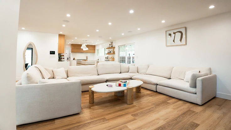 Open-plan living room with a cream sectional, wood flooring, and a view into the kitchen