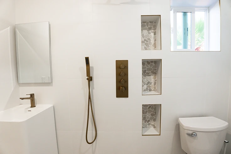 White-tiled bathroom with brass shower fixtures and stacked stone-lined niches