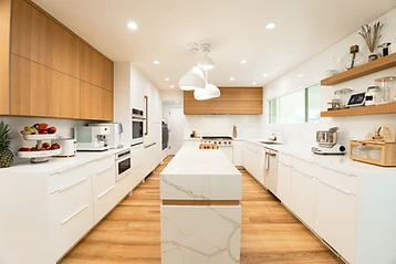Kitchen island framed by white countertops, wood cabinetry, and pendant lights