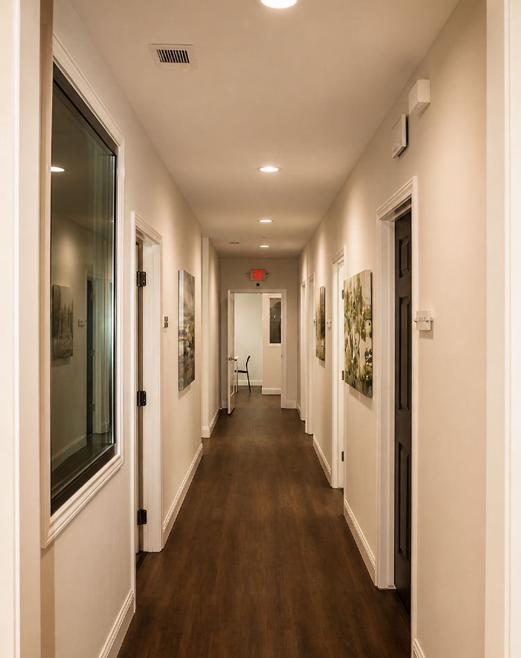 A warm, well-lit ElmWorks office hallway lined with framed artwork and private office doors