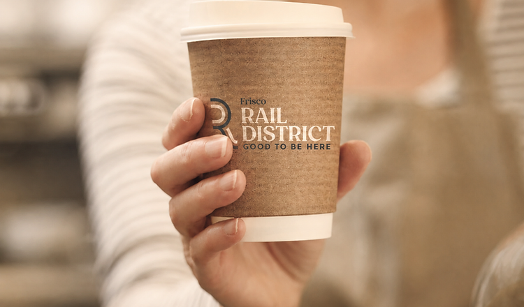 A hand holding a Frisco Rail District coffee cup, capturing the local character of Historic Downtown Frisco