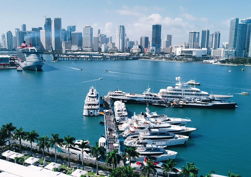 Aerial view of a marina lined with luxury yachts, palm trees and the Miami skyline