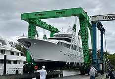 A white yacht lifted by a green Cimolai marine travel lift at a Caribbean dockyard with crew overseeing the lift operation