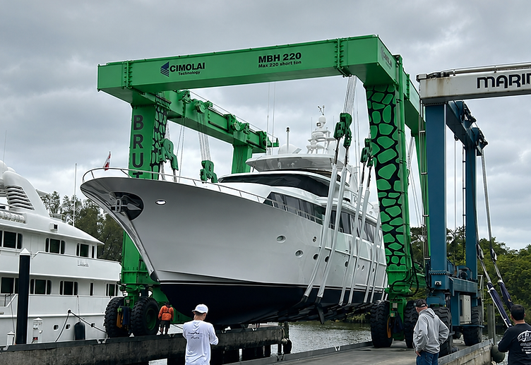 A white yacht lifted by a green Cimolai marine travel lift at a Caribbean dockyard with crew overseeing the lift operation