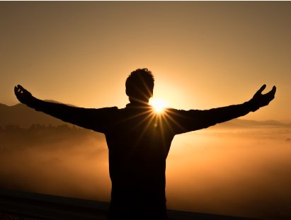A person standing with arms outstretched at sunset