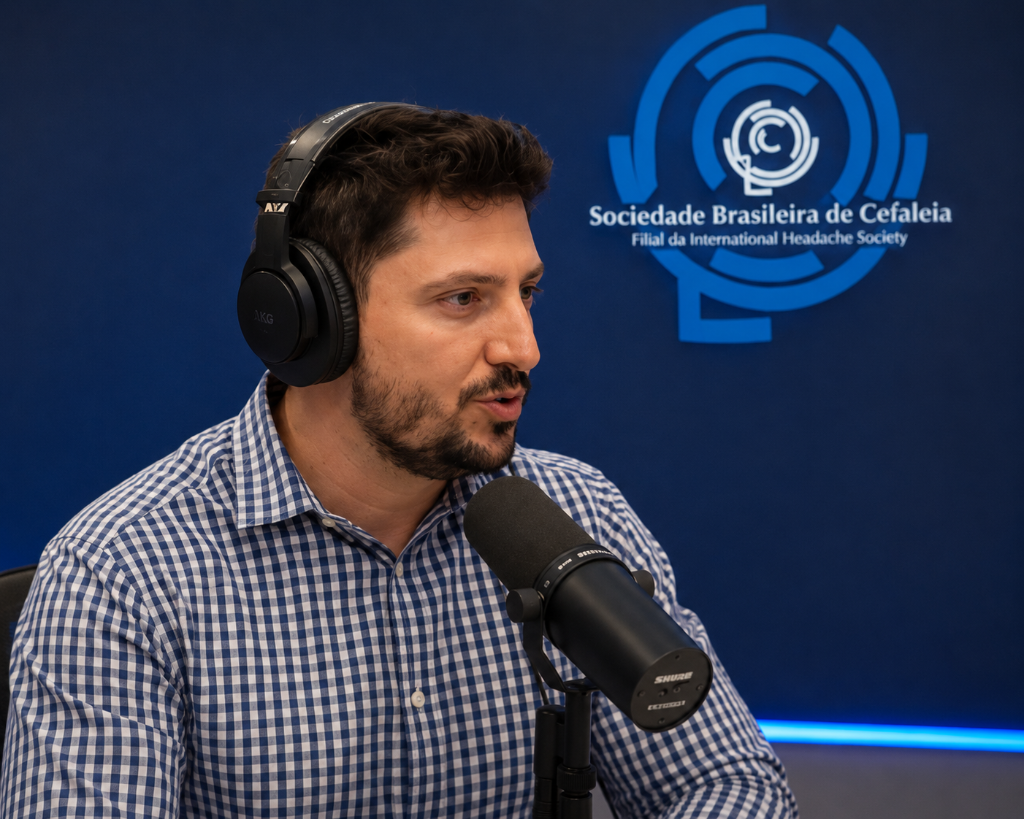 Dr. Marcelo Zalli, médico neurologista, participando de entrevista ou podcast sobre saúde e neurologia, usando microfone de estúdio Shure e fones de ouvido AKG, com o logotipo da Sociedade Brasileira de Cefaleia ao fundo.