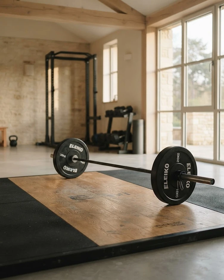 A loaded barbell and weight plates on a platform in a bright, calm gym