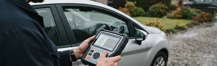 Handheld diagnostic scanner displaying live vehicle data on a driveway