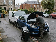 Mobile auto-electrician van parked on a residential street with a car's bonnet open for on-site diagnosis