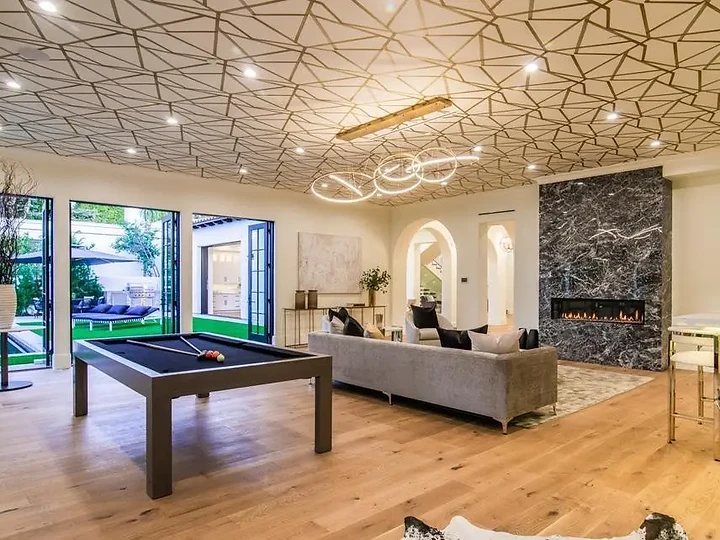 A billiard table under a patterned ceiling, with glass doors folded open to the pool, an interior by Apel Design