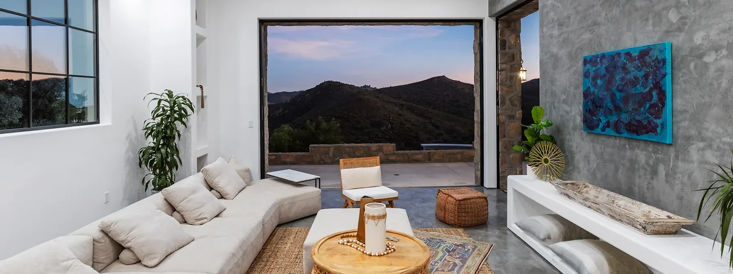 A white sectional and carved round table facing mountains at dusk, at Maliview in the Malibu Mountains, by Apel Design