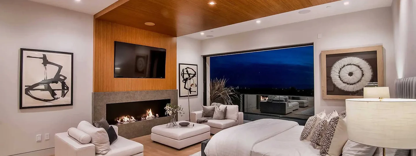 Lounge chairs by a linear fireplace in a wood-lined wall, with glass facing dusk, an interior by Apel Design