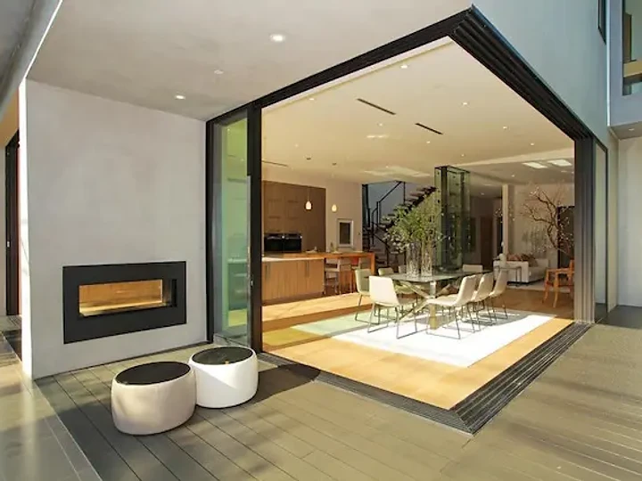 A covered deck and linear fireplace beside an open glass corner to the dining room, an interior by Apel Design