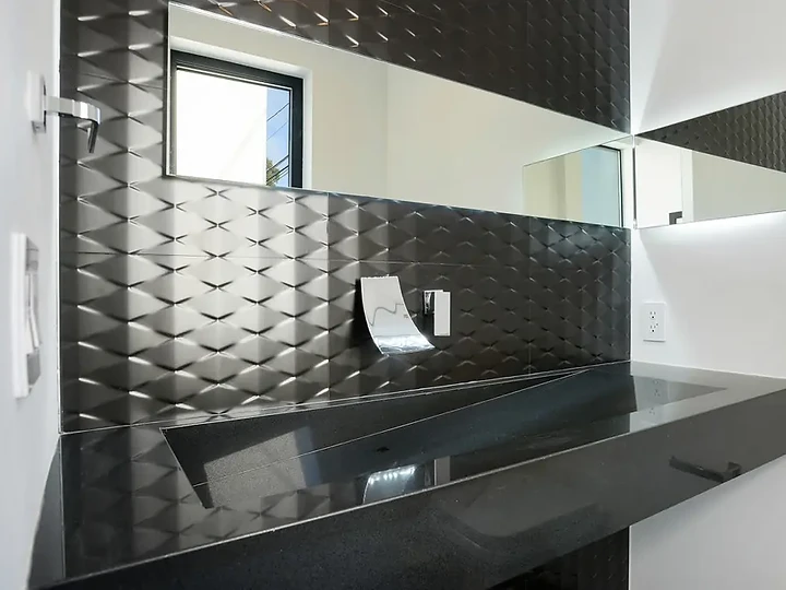 Black dimensional tile wall above a black stone trough sink with a wall-mounted faucet, an interior by Apel Design
