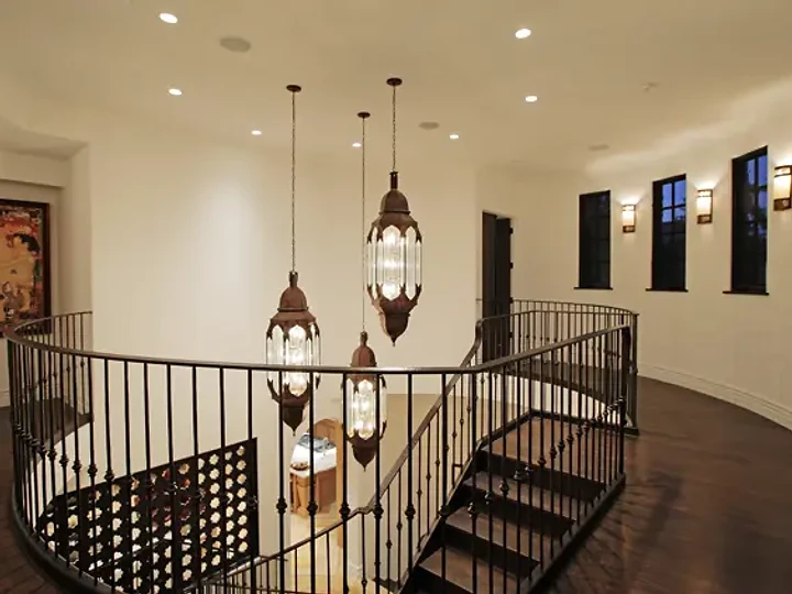 Lantern pendants hanging in a curved stair hall with an iron railing and wall sconces, an interior by Apel Design