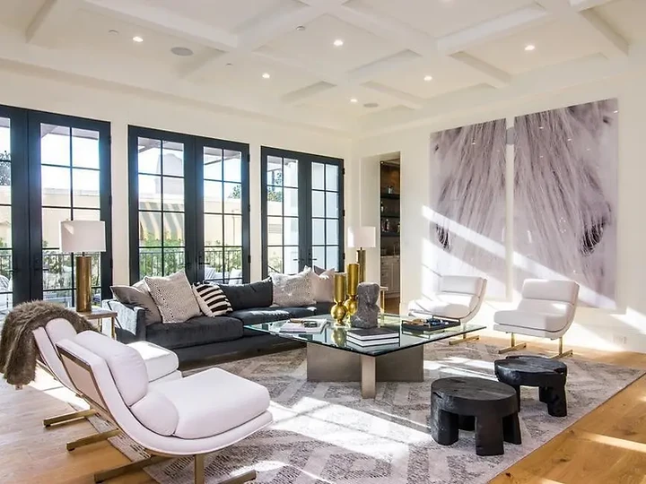 A living room with black steel-framed doors, a coffered ceiling and sculptural lounge chairs, an interior by Apel Design