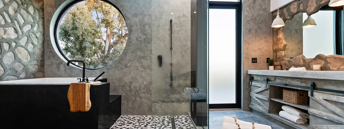 Black tub under a round window beside a stone wall and glass shower, at Maliview in the Malibu Mountains, by Apel Design