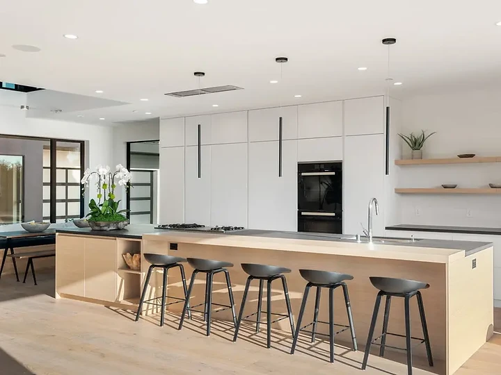 White kitchen with a pale oak island, five stools and open shelves on the back wall, an interior by Apel Design
