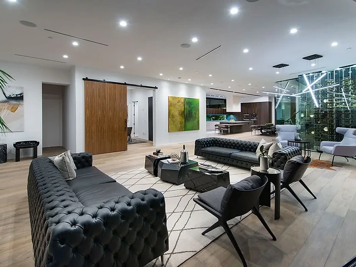 An open great room with tufted leather sofas and a lit glass wine display beyond, an interior by Apel Design